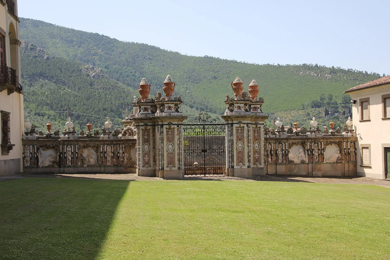 Il cancello barocco decorato con statue e vasi nel cortile della Certosa di Calci, con le pendici boscose del Monte Pisano alle spalle