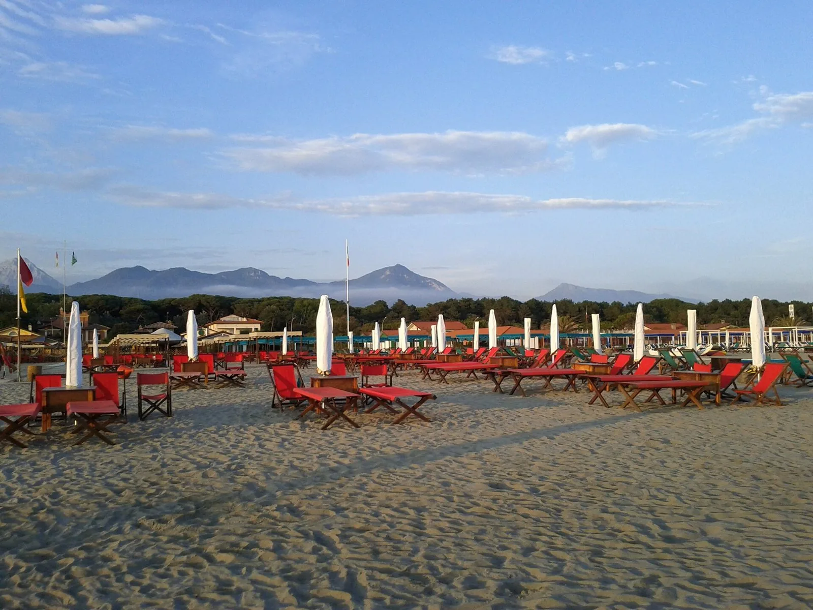 Spiaggia di Forte dei Marmi con sdraio rosse, ombrelloni chiusi e le Alpi Apuane sullo sfondo